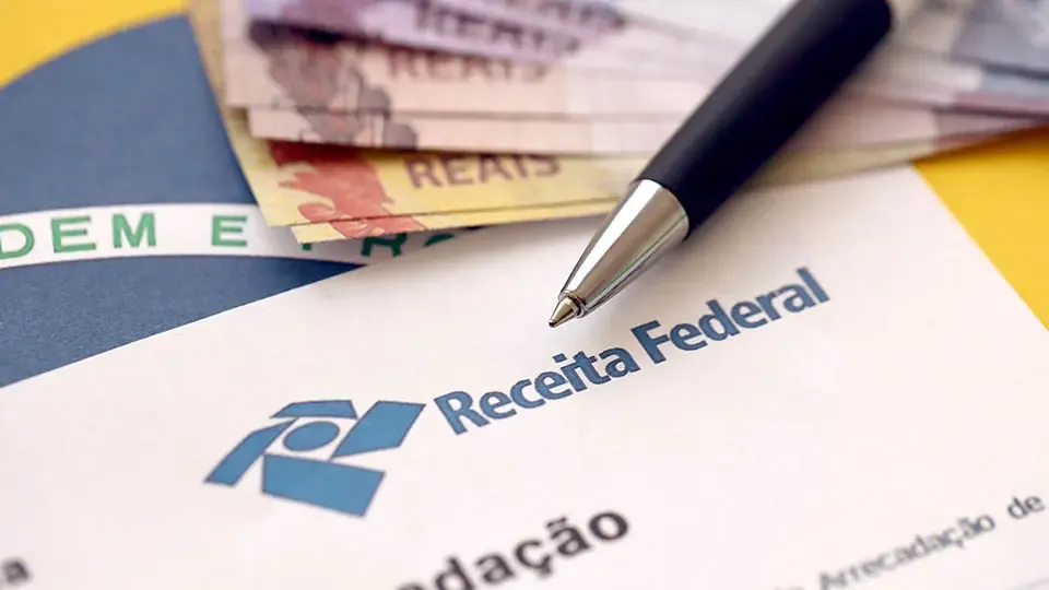 Documento da Receita Federal, caneta e cédulas de real, ilustrando a análise da isenção de Imposto de Renda